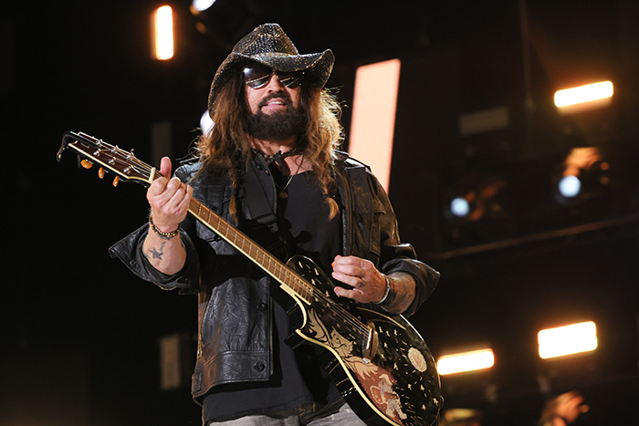 Billy Ray Cyrus in a hat playing guitar on stage.