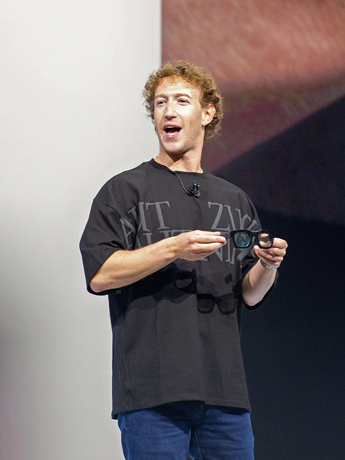 Mark Zuckerberg holding glasses, standing on stage.