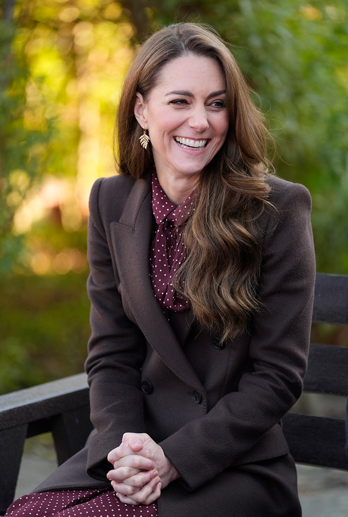 Kate Middleton smiling in a brown coat with earrings, seated outdoors on her 43rd birthday.