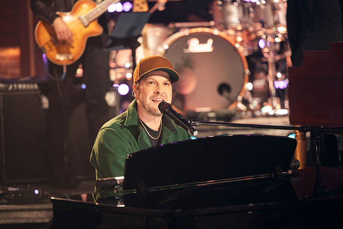 Gavin DeGraw performing at an event, playing piano and singing into microphone on stage.
