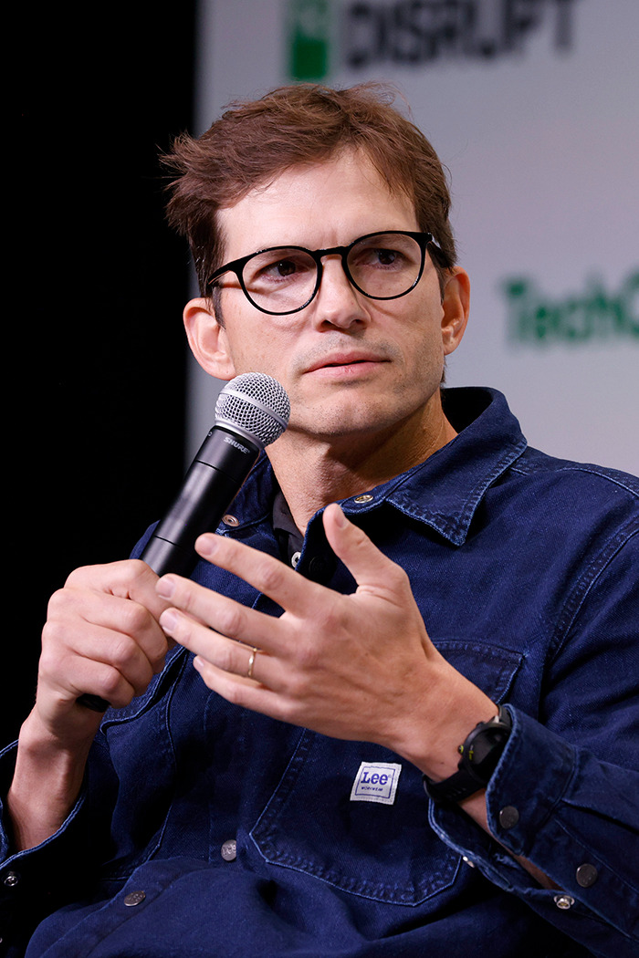 Ashton Kutcher in blue denim jacket holding a microphone.
