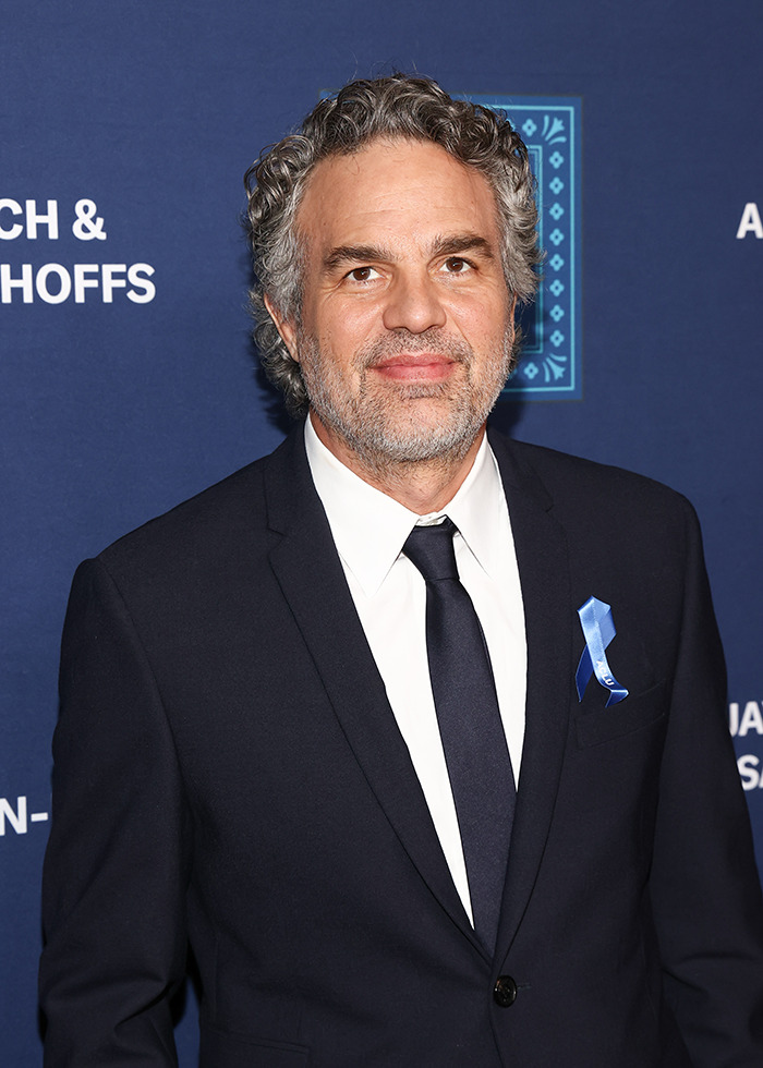 Mark Ruffalo in a suit with a blue ribbon at an event.