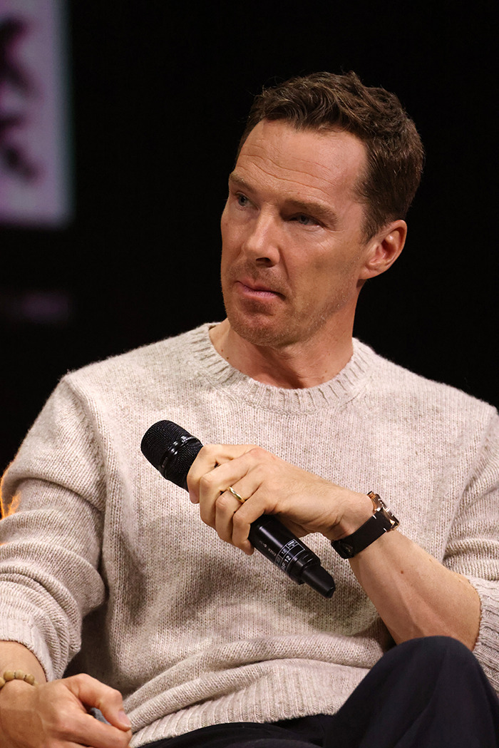 Benedict Cumberbatch speaking into a microphone wearing a beige sweater. Benedict Cumberbatch speaking into a microphone wearing a beige sweater.