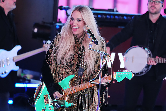 Carrie Underwood performing on stage with a guitar, wearing an embellished outfit.