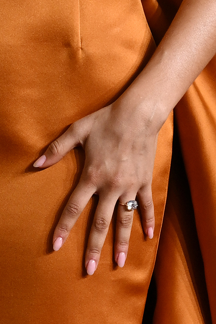 Engagement ring on Zendaya's hand over orange dress.