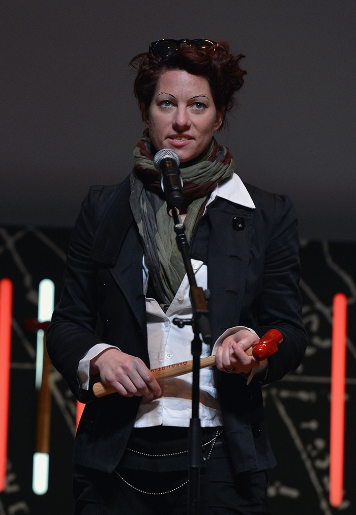 Amanda Palmer in a black jacket and scarf holding a microphone on stage.