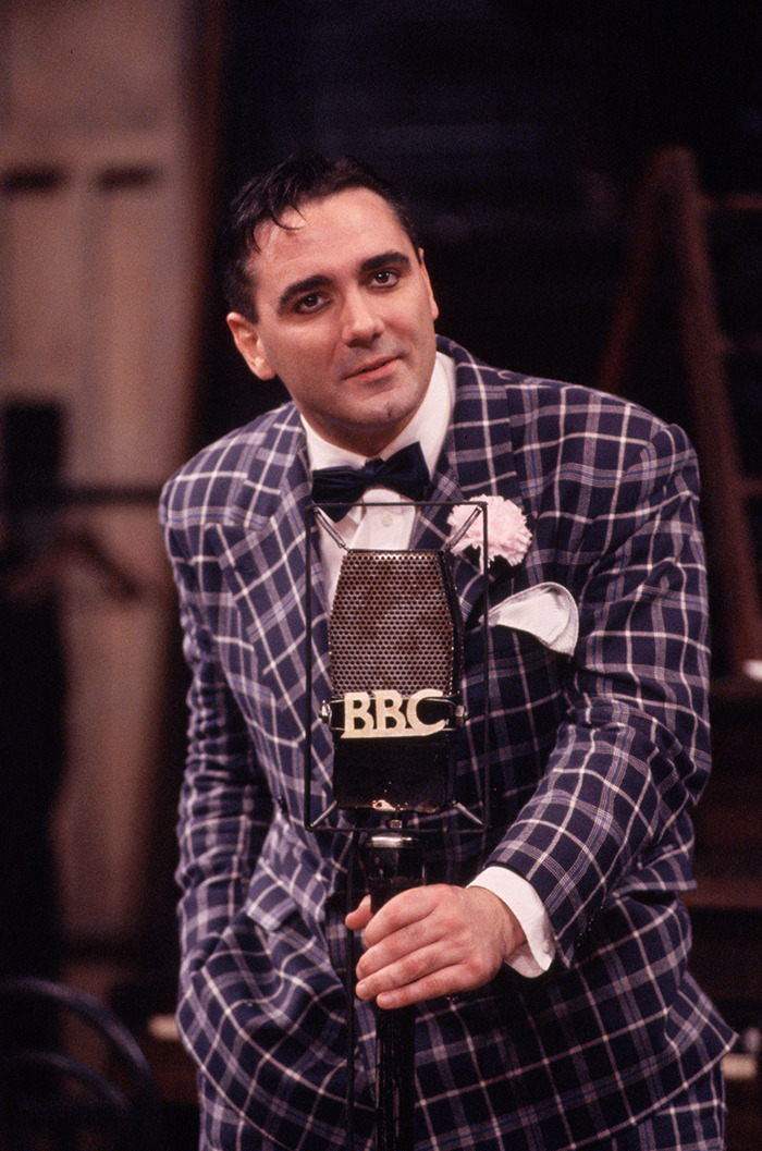 Tony Slattery in plaid suit and bow tie with BBC microphone.