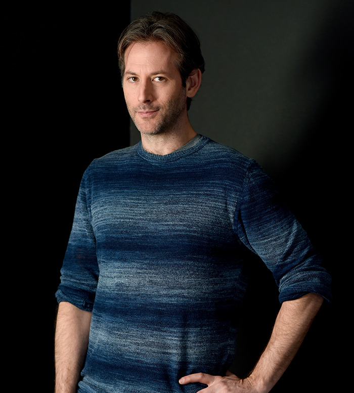 Jeff Baena wearing a blue sweater standing against a dark background. Jeff Baena wearing a blue sweater standing against a dark background.