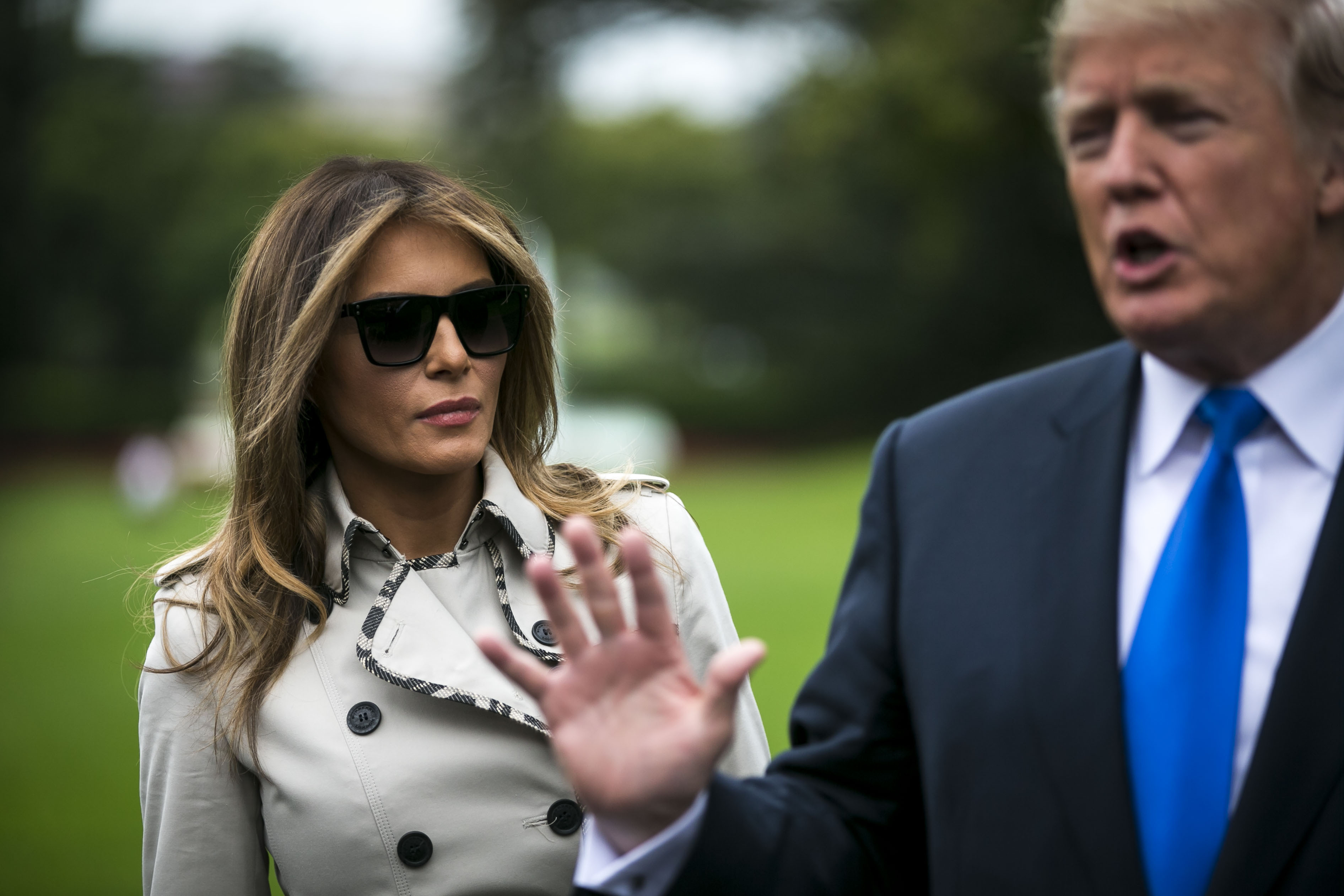 Melania in sunglasses and coat, standing near Trump, sparking "body double" rumors.
