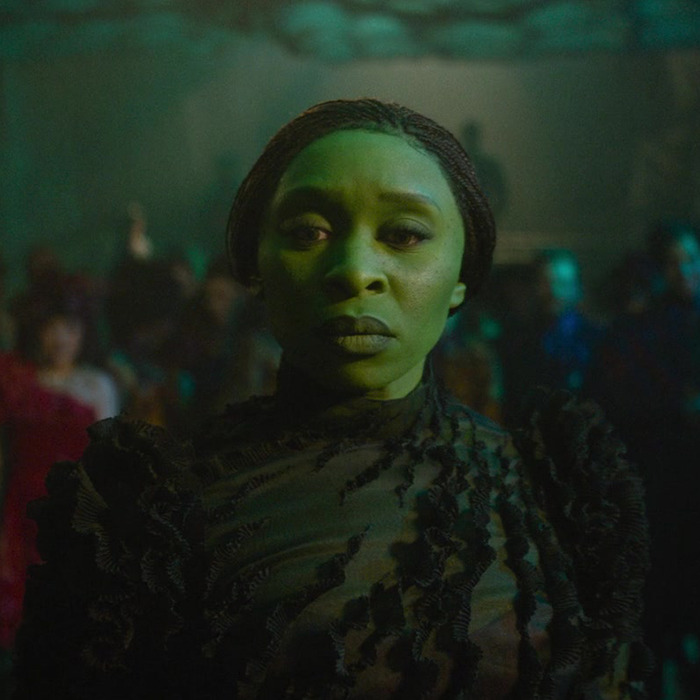 Cynthia Erivo as Elphaba standing in a dimly lit crowd, wearing a textured dark outfit. Cynthia Erivo as Elphaba standing in a dimly lit crowd, wearing a textured dark outfit.