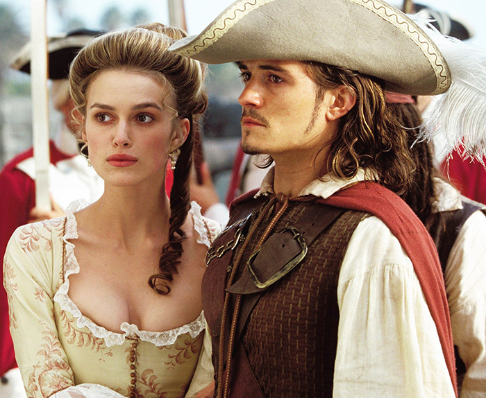 Keira Knightley and Orlando Bloom in period costumes from Pirates of the Caribbean, standing side by side. Keira Knightley and Orlando Bloom in period costumes from Pirates of the Caribbean, standing side by side.