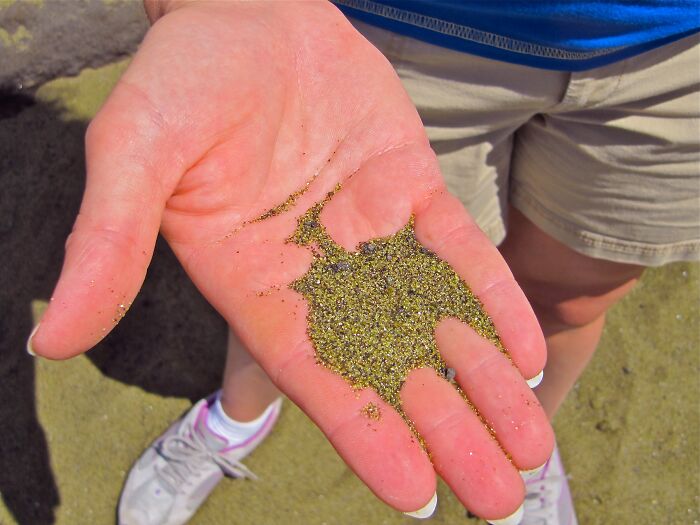 A hand holding green sand, showcasing a stunning natural phenomenon in a beach setting.