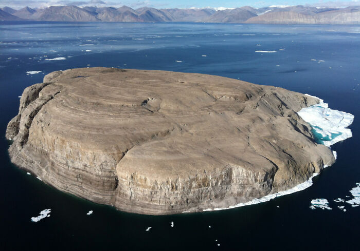 Aerial view of a barren rock island surrounded by icy waters, illustrating overlooked historical events in remote regions.
