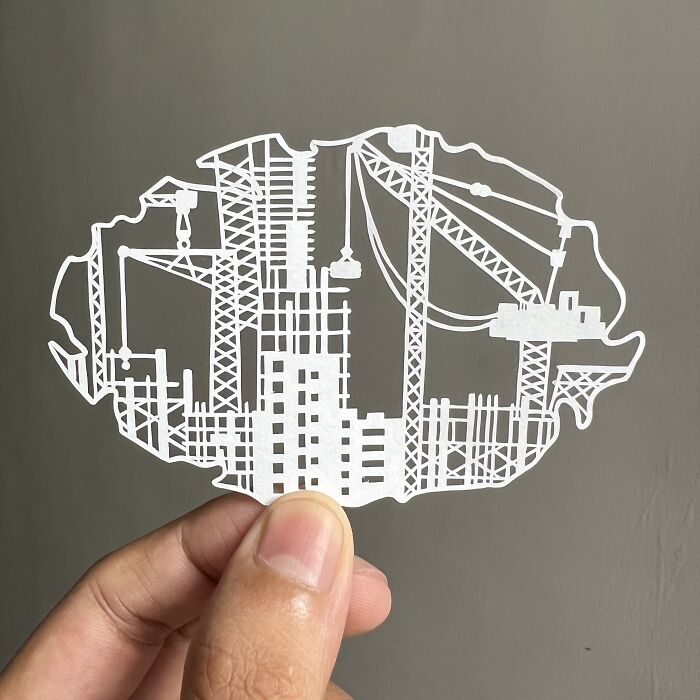 Intricate paper cut design depicting a construction scene, highlighting tree-less existence themes, held by a hand.