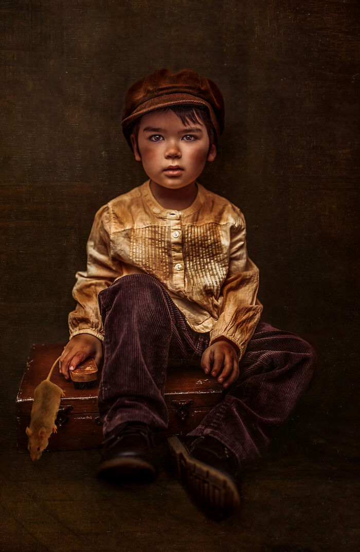 Creative photo of a child sitting on a suitcase, wearing vintage clothes, with a small rat nearby.