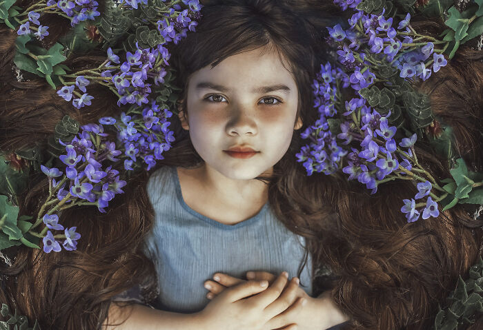 Creative photo of a child lying among purple flowers, wearing a blue dress.