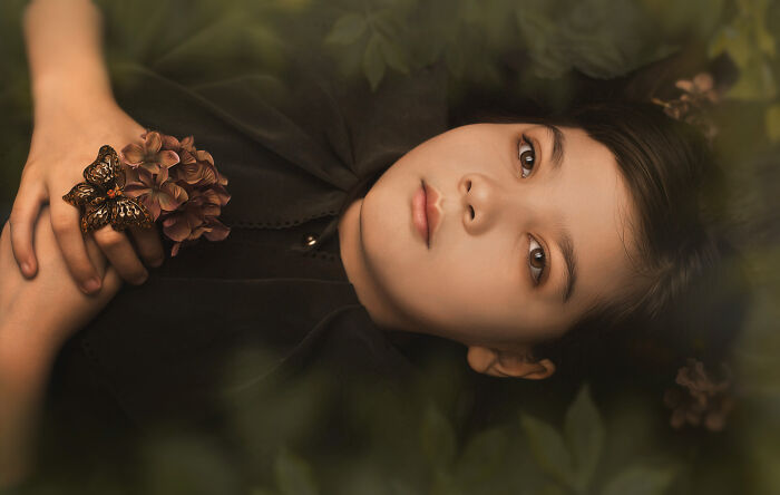 Creative photo of a child lying on foliage, holding flowers, expressing emotion and imagination.