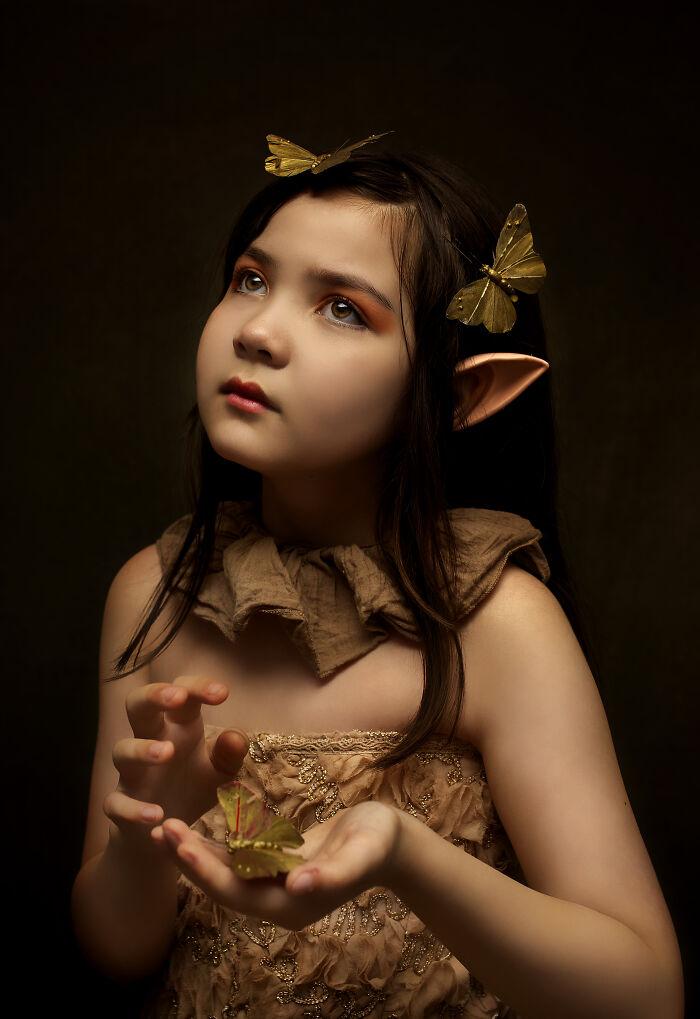 Child with butterfly-themed accessories and elfin ears, looking upward creatively.