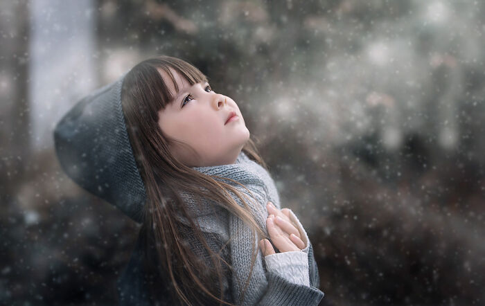 Child in a winter scene gazing upwards, wearing a gray hat and scarf, capturing a creative photo moment.