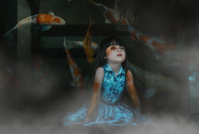 A child in a blue dress sits surrounded by koi fish, illustrating a creative photography concept.