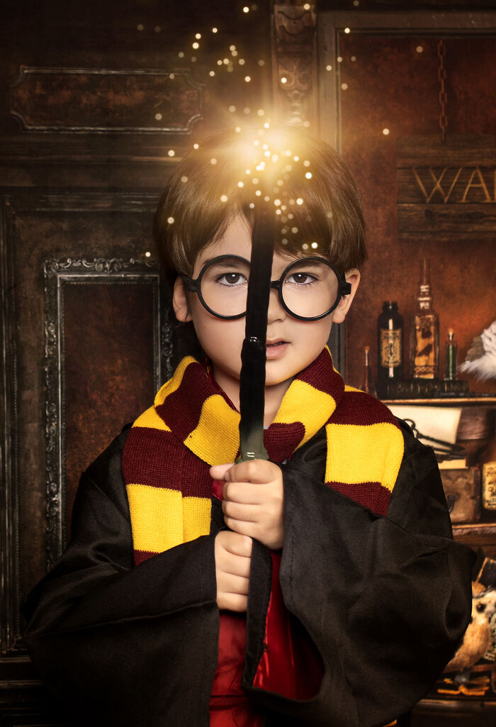 Creative photo of child in wizard costume holding glowing wand, wearing round glasses and striped scarf.