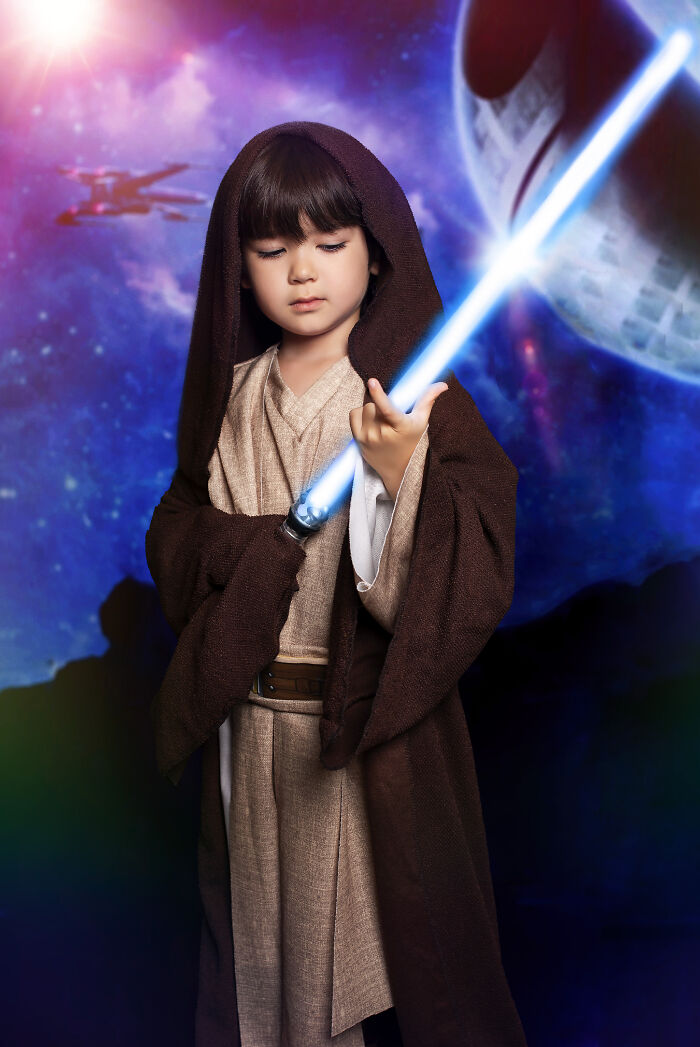 Creative photo of a child dressed as a Jedi holding a lightsaber with a galaxy background.