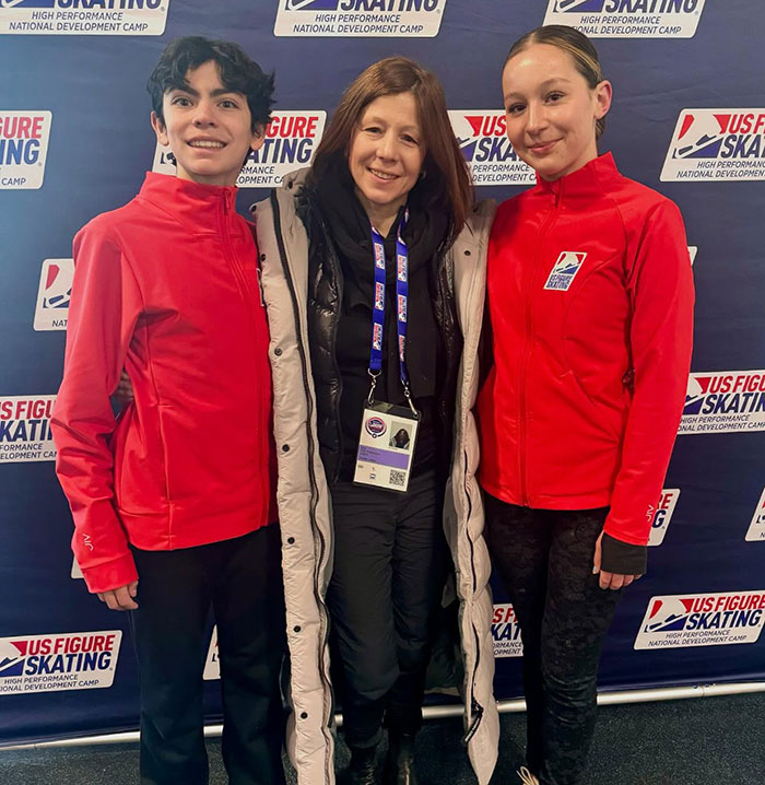 Three individuals smiling at a US Figure Skating event, with two wearing red jackets, highlighting 'Disney On Ice' actress.