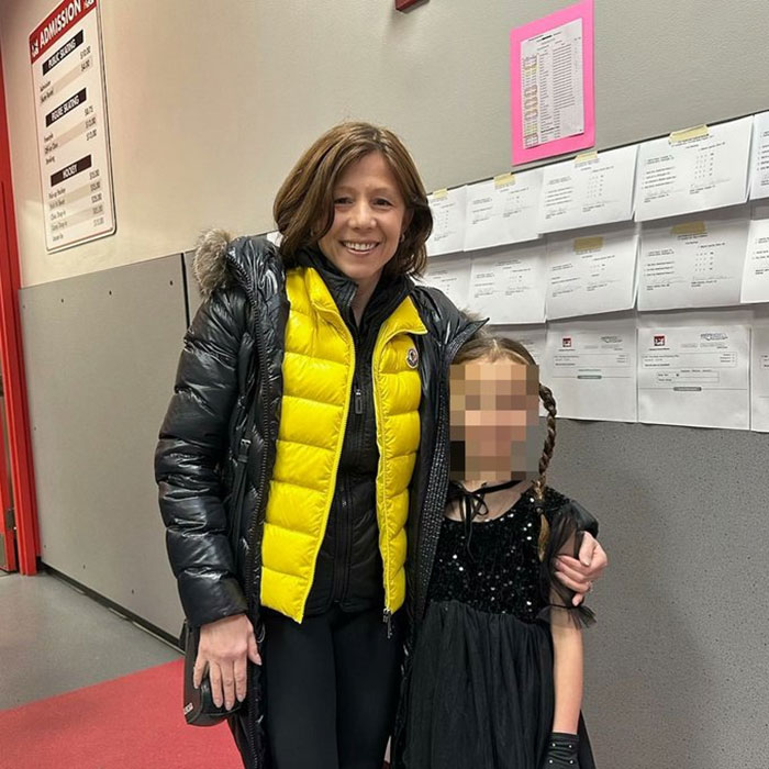 Woman in a yellow jacket, smiling next to a child in a black dress, indoors.
