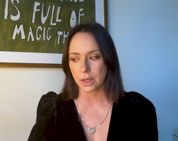 A woman in a black top sits under a framed sign, discussing experiences with grown men commenting on her at 16.