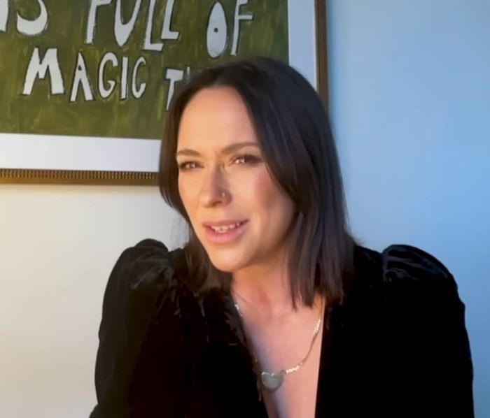 Woman in a black top sitting in front of a framed artwork, discussing issues related to media and her career.