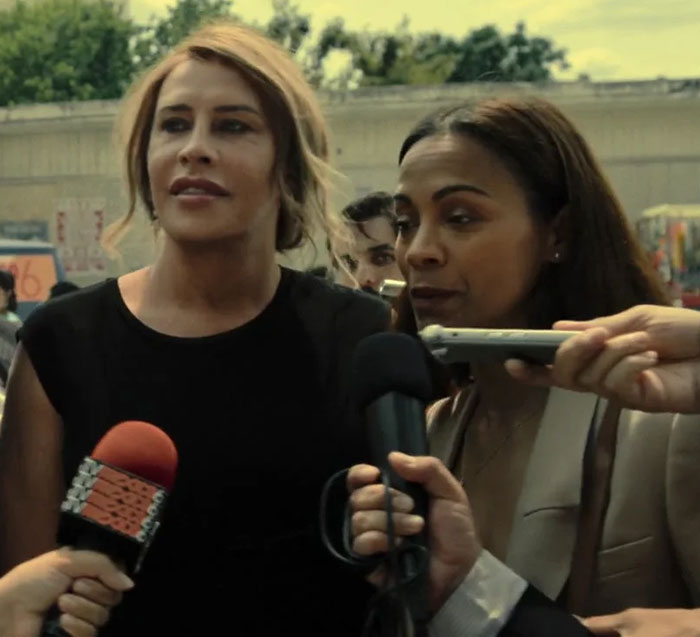 Transgender Oscar nominee speaking to press, surrounded by microphones, addressing resurfaced posts controversy.