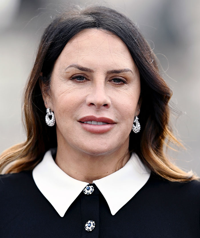 Transgender Oscar nominee with dark hair, wearing gemstone earrings and a black dress with a white collar.