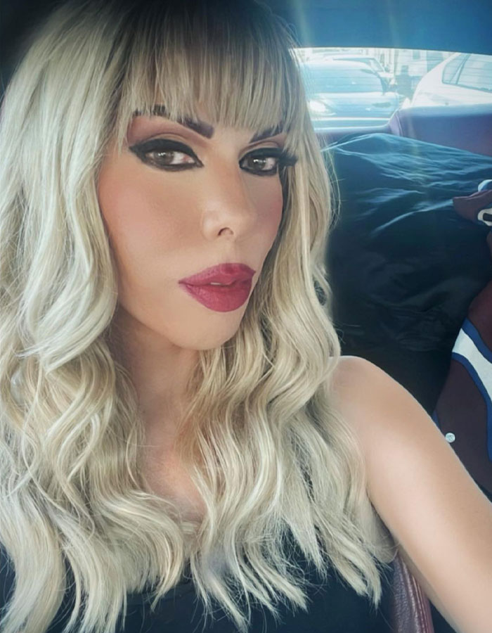 A person with long blonde hair and bold makeup taking a selfie in a car. A person with long blonde hair and bold makeup taking a selfie in a car.