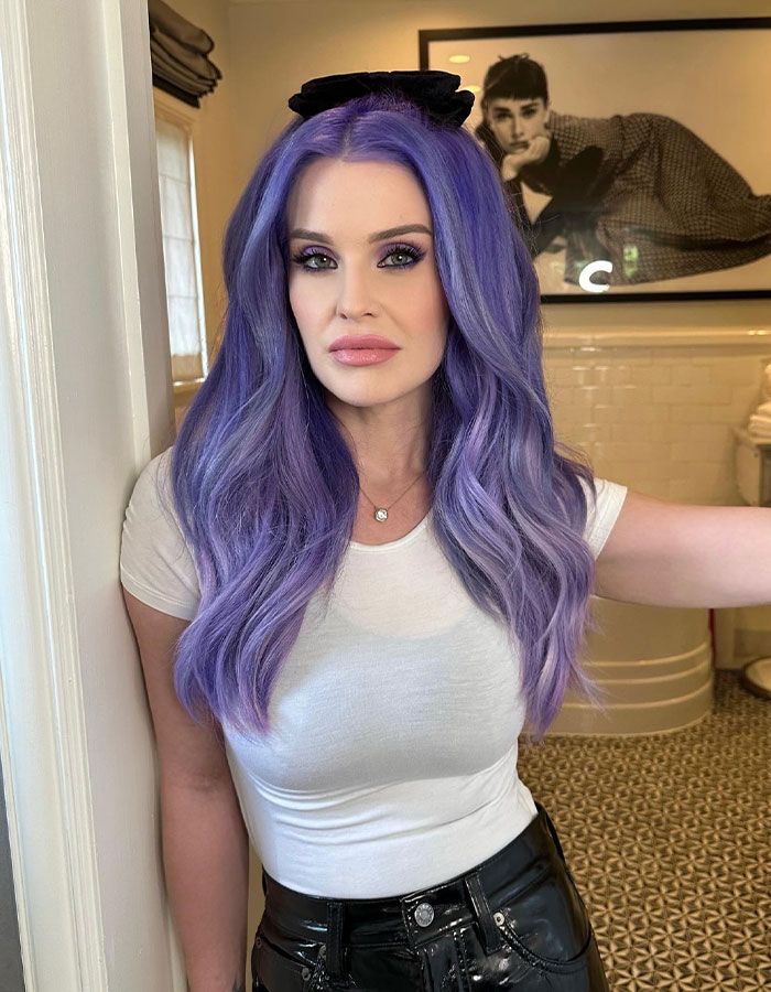 Purple-haired woman in a white top stands indoors, highlighting concerns over celebrity photo ops during LA fires.