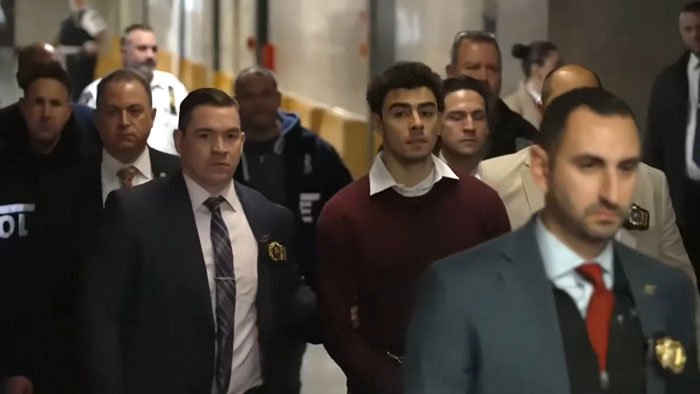 A man escorted by police officers in a corridor related to UnitedHealth value loss incident. A man escorted by police officers in a corridor related to UnitedHealth value loss incident.