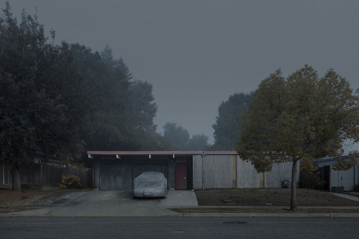 Suburban house on a foggy day, car covered in driveway, illustrating suburban disconnection.