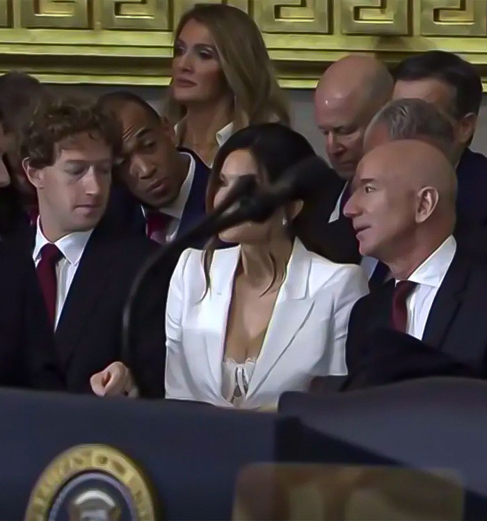 Group of people sitting at an event, one person looking towards the woman in white amid others in formal attire.