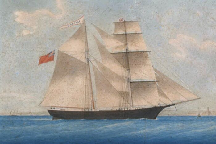 Historic ship at sea, linked to weird unsolved mysteries, sails under a clear sky with a red flag on its mast.