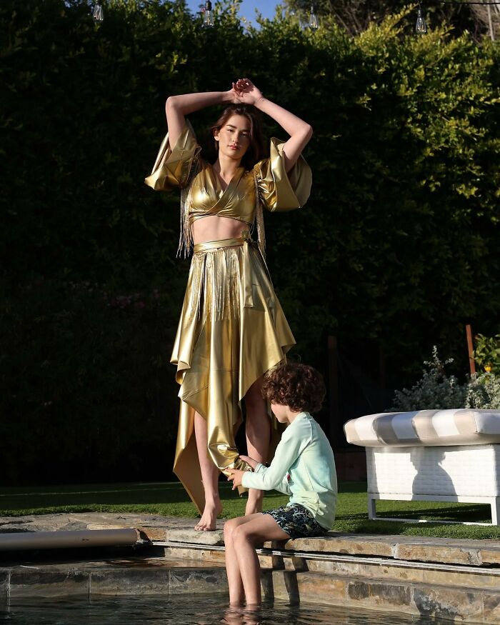 Fashion prodigy in a gold dress poses by the pool, designed for a runway show by an 8-year-old.