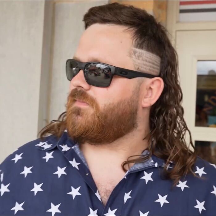Man with a stylish mullet hairstyle, wearing sunglasses and a star-patterned shirt, showcasing the mullet trend.