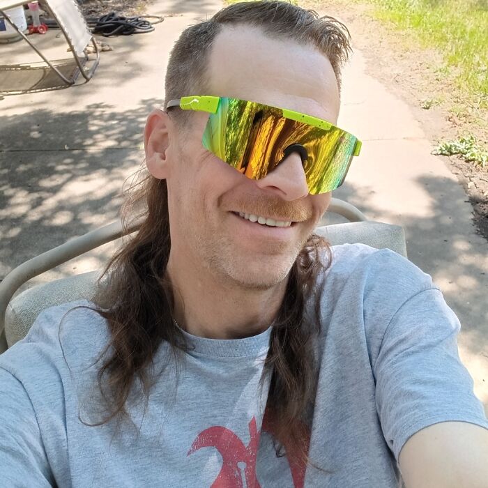 Person wearing reflective sunglasses and a mullet hairstyle outdoors, embodying the party in the back 2024 trend.