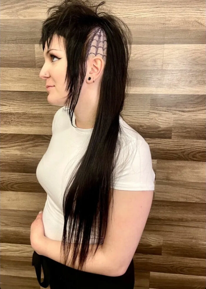 Person with creative mullet hairstyle featuring spiderweb design on the side, wearing a white shirt.