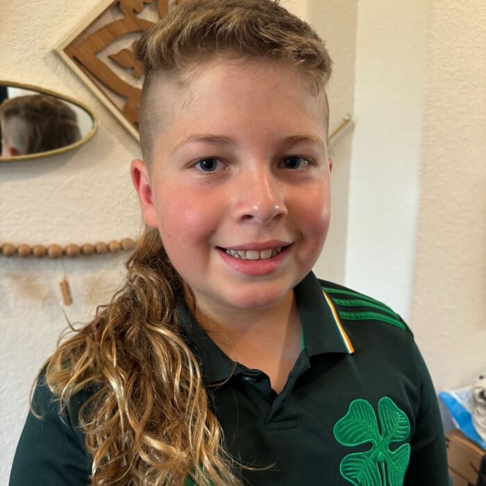 Young person with a stylish mullet hairstyle, combining short top and long curly back, wearing a green shamrock shirt.