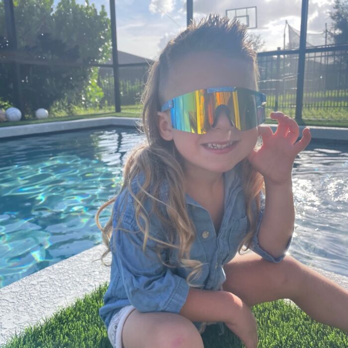 Child by the pool wearing sunglasses, showcasing a trendy mullet hairstyle.