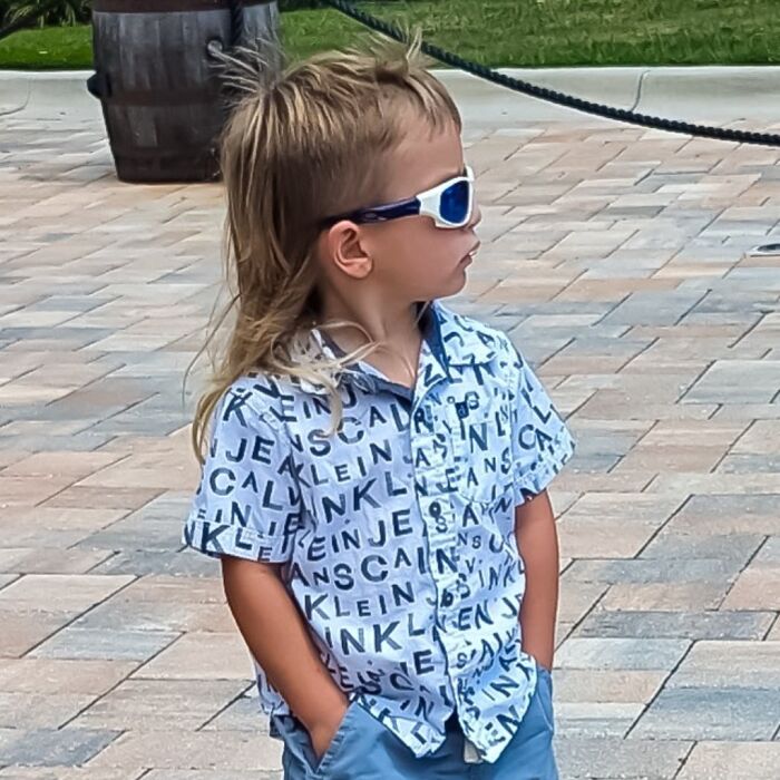 Child wearing sunglasses with a trendy mullet hairstyle, embodying the "Business In The Front, Party In The Back" look.