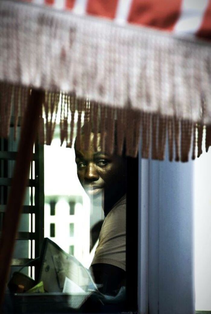 A person looks out through a glass window, capturing an everyday moment through Nadia Eeckhout’s lens.