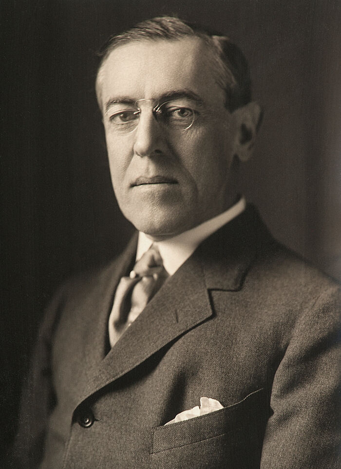A man in a suit and glasses, posing for a formal black and white portrait.