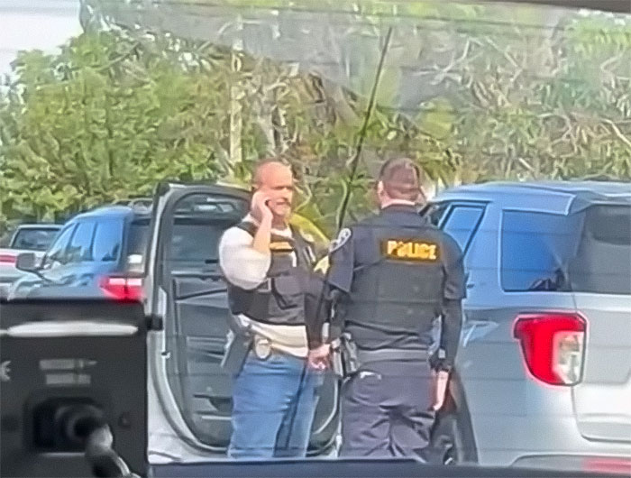 Police officers at a scene involving school principal arrest, outdoors near vehicles. Police officers at a scene involving school principal arrest, outdoors near vehicles.