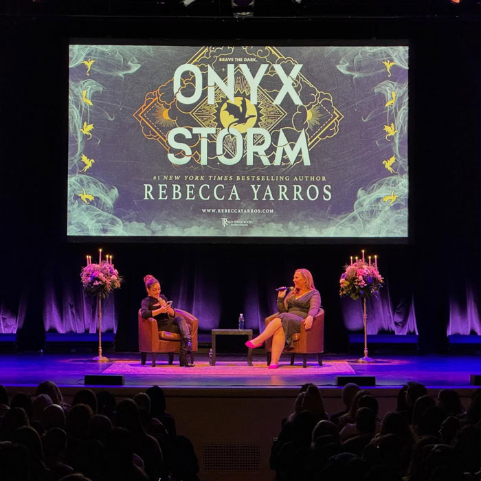 Authors discussing spicy romantasy novels on stage, with "Onyx Storm" book cover displayed prominently behind them.