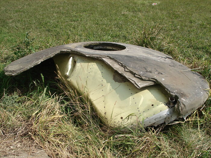 Damaged metal object in a grassy field, possibly related to overlooked historical events.